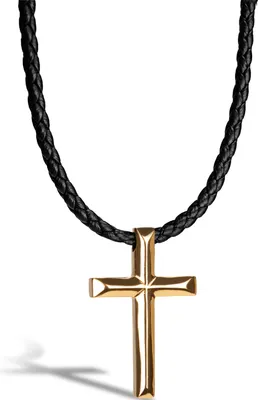 A close-up studio shot of a gold cross pendant on a black braided leather necklace against a white background.