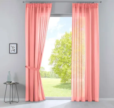 Two coral-colored sheer curtains are drawn to the sides of a window, revealing a green tree and a blue sky outside. A small side table with a bottle on it is visible to the left.