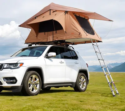 A white SUV with a rooftop tent is parked on a grassy field with mountains in the background.