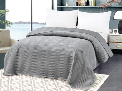 A neatly made bed with a grey blanket, white pillows, and a patterned rug in a bedroom setting.
