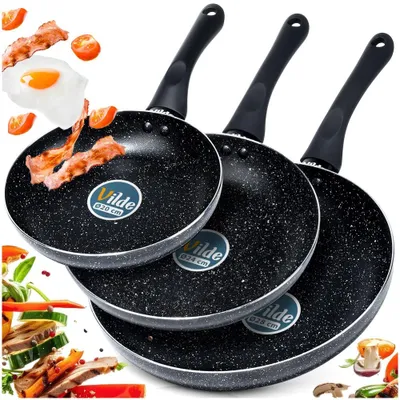 Three frying pans of different sizes are arranged diagonally, with some food items like bacon, eggs, and vegetables scattered around them.