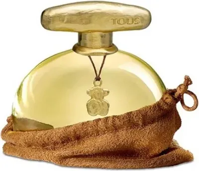 A perfume bottle with a gold cap and a small teddy bear charm hanging from it, partially covered by a brown fabric pouch.