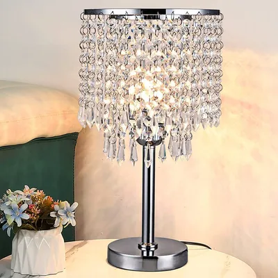 A crystal table lamp is placed on a table next to a pillow and a vase of flowers.