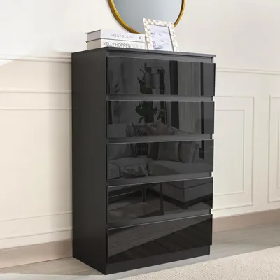 A black chest of drawers with glossy black drawer fronts, placed against a wall with decorative molding.