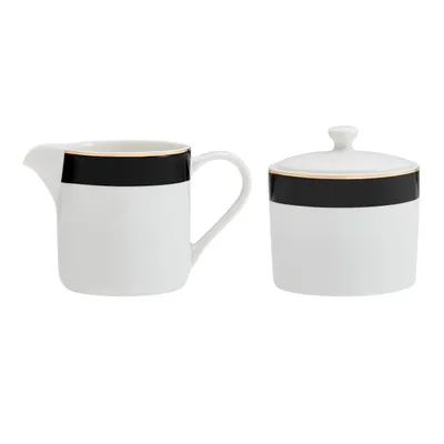 A white sugar bowl with a lid and a white creamer pitcher, both with a black band and a thin gold trim, are displayed against a white background.