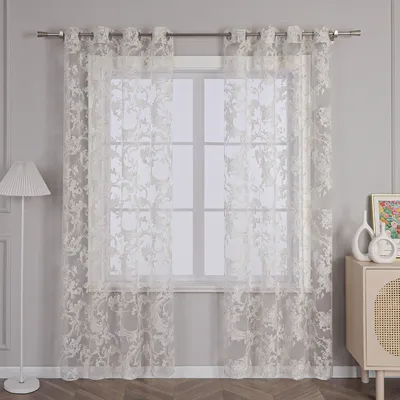 A sheer, white lace curtain with a floral pattern hangs in front of a window.