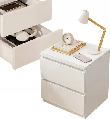 A white nightstand with two drawers, one of which is open, showing headphones and a phone. On top of the nightstand is a lamp, a clock, and two books. A second, open nightstand is visible in the background.