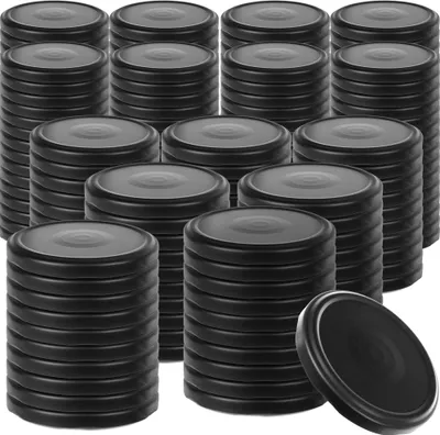 Stacks of black screw-on lids for jars, with one lid shown tilted in the foreground.