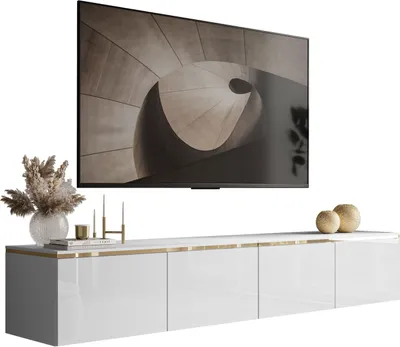 A modern white TV cabinet with gold trim, mounted on a wall, with a large flat-screen TV above it displaying abstract art. Decorative items like a vase with dried flowers, candles, and spheres are placed on the cabinet.