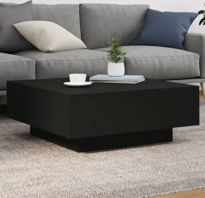 A black coffee table with a cup and a plant on it, placed in front of a gray sofa.