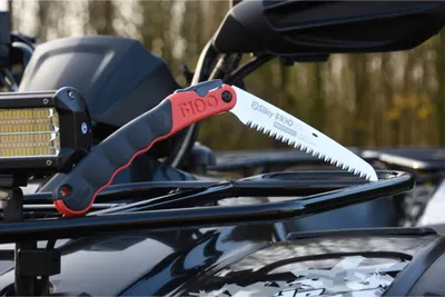 A folding saw is placed on the rack of an ATV.
