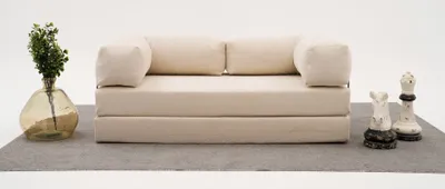A cream-colored sofa is displayed on a gray rug against a white background, with a vase of greenery on the left and chess pieces on the right.