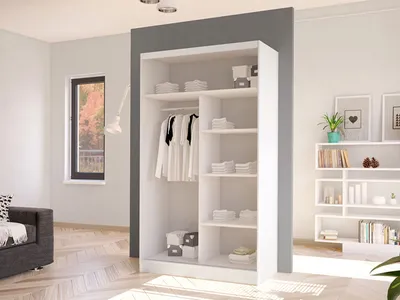 A white wardrobe with sliding doors is shown in a room with light-colored walls and wooden flooring. The wardrobe is open, revealing shelves with folded clothes and a hanging rail with shirts.