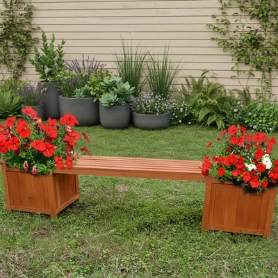 A garden bench with integrated planters filled with red flowers, set in a grassy yard with a wooden fence in the background.