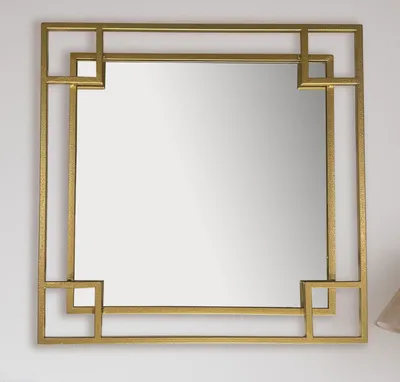 A square gold metal framed mirror with a geometric design, hung on a white wall.