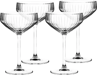 Four clear champagne coupe glasses with vertical ribbed detailing are arranged on a white background.