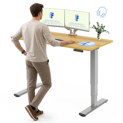 A man is standing at a height-adjustable desk with two monitors.