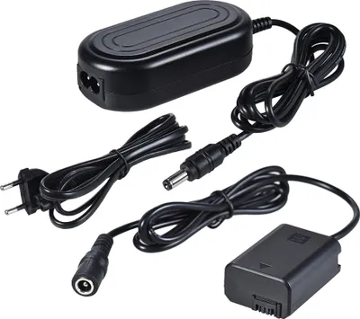 A black camera battery charger and dummy battery adapter kit is laid out on a white background.