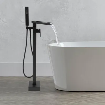 A black freestanding bathtub faucet with a handheld showerhead is filling a white bathtub.