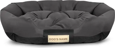 A dark gray dog bed with a lighter gray cushioned interior and a small beige tag with the words "DOG'S NAME" printed on it.