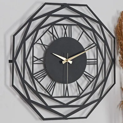 A black geometric wall clock with Roman numerals and gold hands is mounted on a light gray wall.