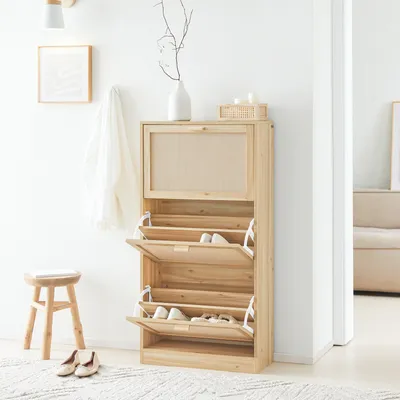 A wooden shoe cabinet with three flip-down drawers is shown in a well-lit room, with a stool and shoes nearby.