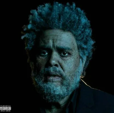 A close-up portrait of an older man with graying hair and beard, looking directly at the camera with a somber expression. The lighting is dramatic, with a blueish tint and a strong highlight on the right side of his face.