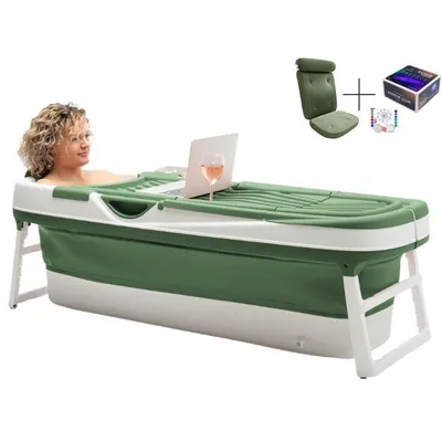 A woman is relaxing in a green and white foldable bathtub with a laptop and a glass of wine.
