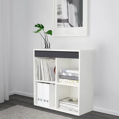 A white shelving unit with books and binders inside, placed against a white wall with a framed picture above.