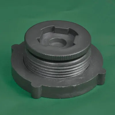 A black plastic cap with threaded edges and a hexagonal opening on top, placed on a green surface.