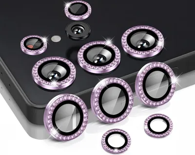 A collection of camera lens protectors with decorative rhinestones arranged on a dark surface, possibly a phone.