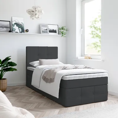 A single bed with a dark gray upholstered base and headboard is shown in a bright room.
