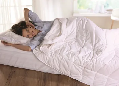 A woman is stretching in bed under a white duvet.