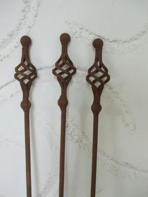 Three rusty metal garden stakes with twisted decorative tops stand against a textured white wall.