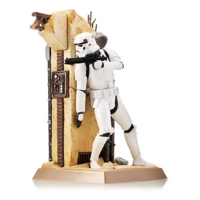 A Star Wars Stormtrooper figurine is posed leaning against a desert-themed structure, holding a blaster rifle.