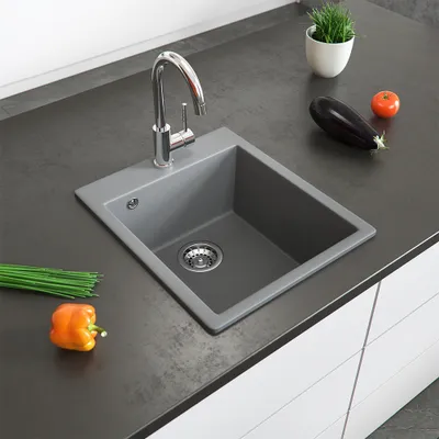 A kitchen sink with a faucet, countertop, and some vegetables.