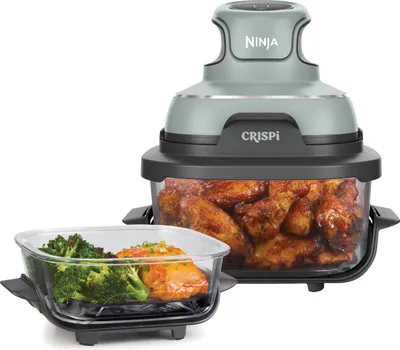 A Ninja CRISPi air fryer with a clear container filled with chicken wings and a separate glass dish containing broccoli and salmon.