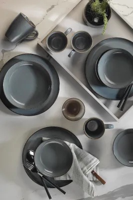 A collection of gray and blue ceramic tableware, including plates and mugs, arranged on a marble-like surface.