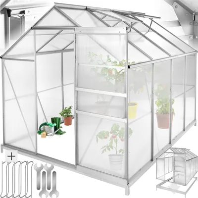 A greenhouse with plants inside, showing its structure and sliding door. Tools and a smaller greenhouse model are also visible.