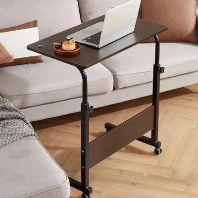 A laptop table with a laptop and a small dessert on it, placed next to a sofa.