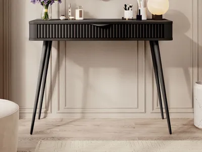 A black console table with fluted drawers and tapered metal legs, decorated with a vase of purple flowers and various cosmetic items.