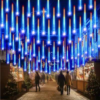 A street scene at night decorated with colorful LED meteor shower lights, with people walking and Christmas trees on display.
