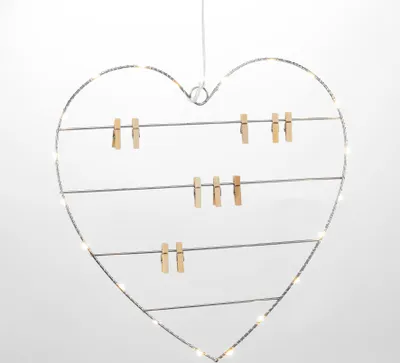 A heart-shaped wire frame with strings and clothespins, decorated with LED lights, hanging against a white background.