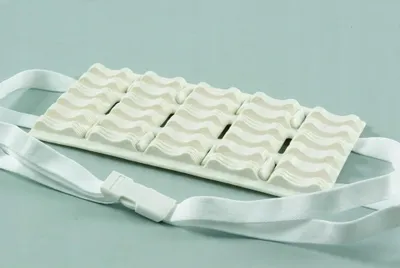 A white massage belt with wavy patterns and white straps with a buckle, lying on a light blue background.