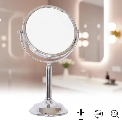 A silver vanity mirror on a stand, placed in a bathroom setting with blurred background elements.