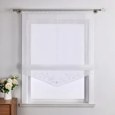 A white sheer curtain with a decorative embroidered hem hangs on a window.