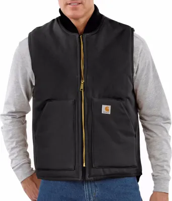 A man wearing a black Carhartt vest over a grey long-sleeved shirt and blue jeans.