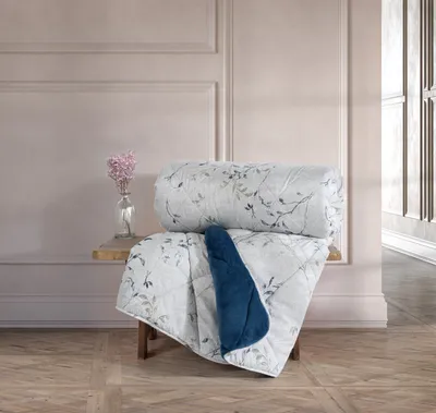 A rolled-up comforter with a floral pattern is displayed on a wooden stool in front of a wall with decorative molding.