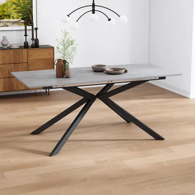 A dining table with a concrete-look top and black metal legs, set in a modern dining room with a wooden sideboard and a chandelier.