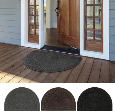 A half-moon shaped doormat placed on a wooden porch in front of an open wooden door.